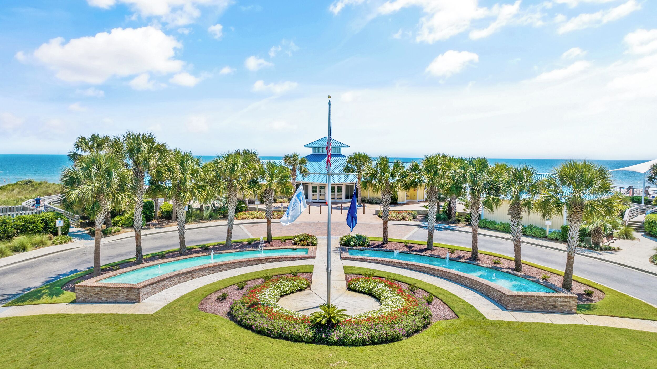A resort with a central pool, palm trees, and a view of the ocean.