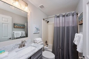 A bathroom with a marble sink, a toilet, a shower with a grey curtain, and a large mirror.