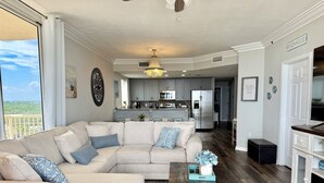 Una sala de estar con un sofá seccional, una mesa de centro y vistas a la cocina y al balcón.