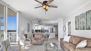A spacious living area with a balcony, a ceiling fan, a glass coffee table, and a brown sofa. - Gulf Front Beach Club - Renovated Corner Condo, Direct Gulf Views! Pool, WIFI (Gulf Shores)
