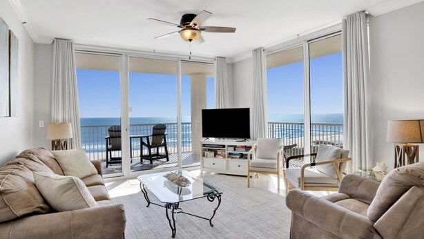 A spacious living room with a large TV, comfortable seating, and a balcony with a view of the ocean. - Gulf Front Beach Club - Renovated Corner Condo, Direct Gulf Views! Pool, WIFI (Gulf Shores)