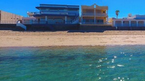 A beachfront property with a clear view of the ocean, a sandy beach, and a multi-story building with balconies.