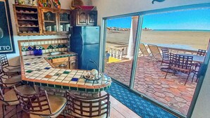 A kitchen with a view of the beach, a bar area with chairs, and a tiled floor.