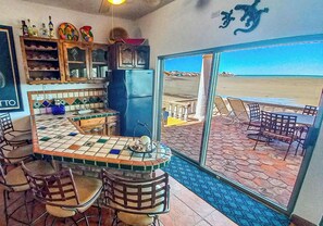 A kitchen with a view of the beach, a bar area with chairs, and a tiled floor.