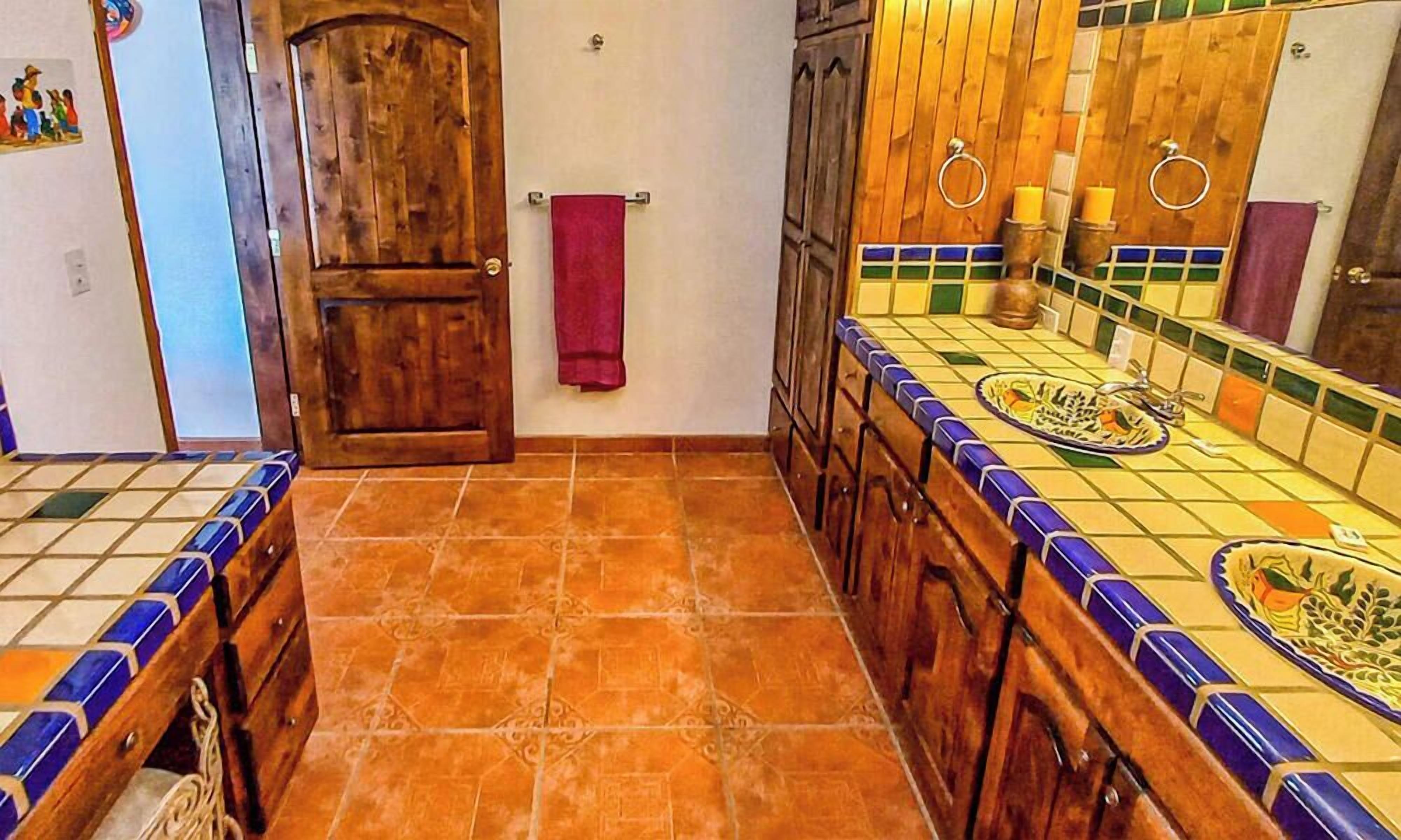 Casa de banho com porta de madeira, chão em mosaico e lavatório com painel decorativo de azulejos.