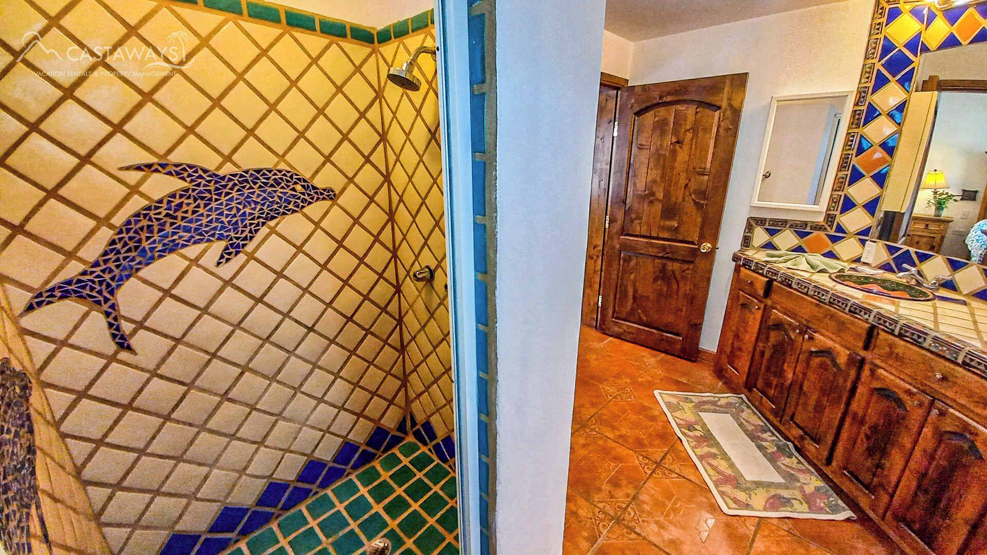 Ein Badezimmer mit Duschboden aus Delfin-Mosaik, einer Holztür und gefliestem Boden.