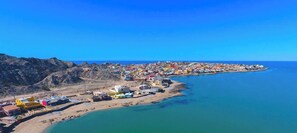A coastal town with buildings along the shoreline, a clear blue sky, and a calm sea.