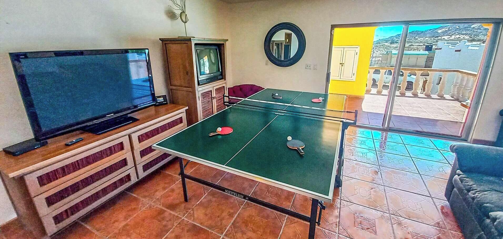 A room with a television, a table tennis table, a cabinet, and a view of a balcony.