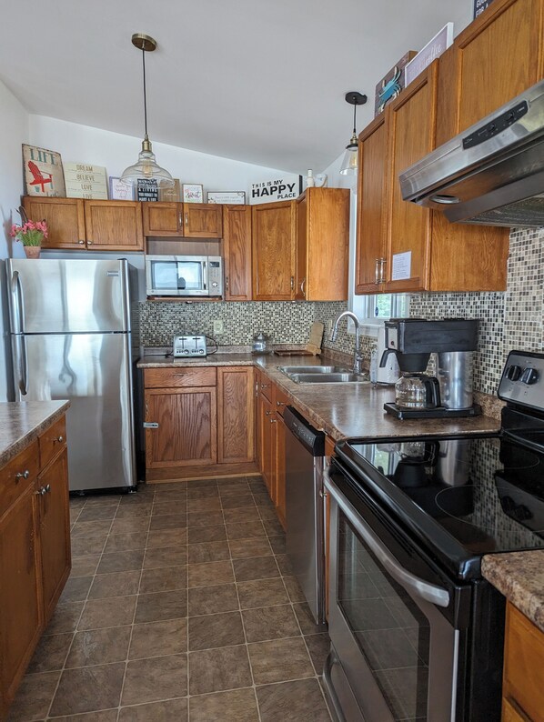 A kitchen with wooden cabinets, stainless steel appliances, a tiled backsplash, and a hanging light fixture. - Stunning Lake Erie Water Views from Every Window with Expansive Patio Deck
(Leamington)