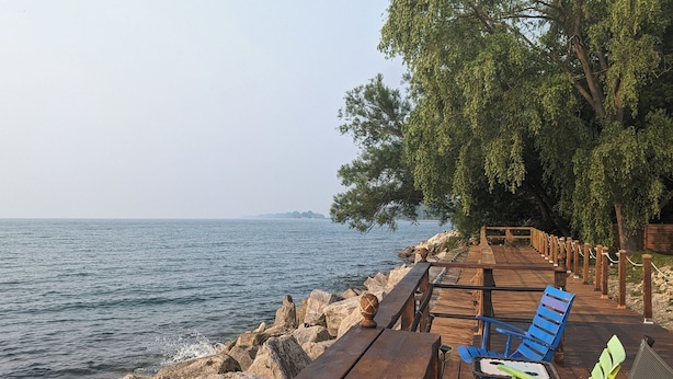 A wooden deck with chairs and a table overlooking a rocky shoreline and the sea.