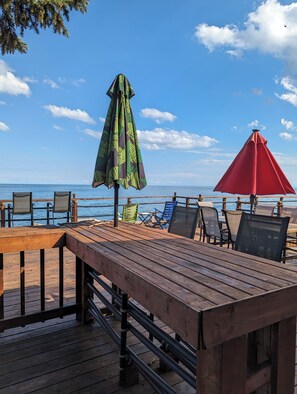 A wooden deck with outdoor seating and umbrellas overlooking a body of water. - Stunning Lake Erie Water Views from Every Window with Expansive Patio Deck
(Leamington)