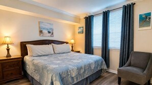 A bedroom with a bed, nightstands, a chair, and a window with curtains.