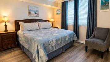 Un dormitorio con cama, mesitas de noche, una silla y un ventanal con cortinas.