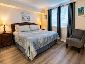 A bedroom with a bed, nightstands, a chair, and a window with curtains.