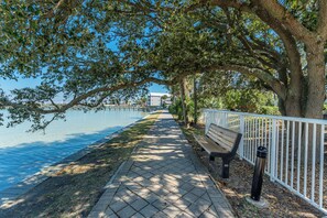 A paved walkway beside a body of water, with a bench and a white fence.