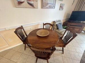 Un comedor con una mesa redonda de madera, seis sillas y un mantel tejido.