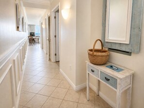 A hallway with a dining area in the distance, a wall-mounted basket, and a small table with drawers.