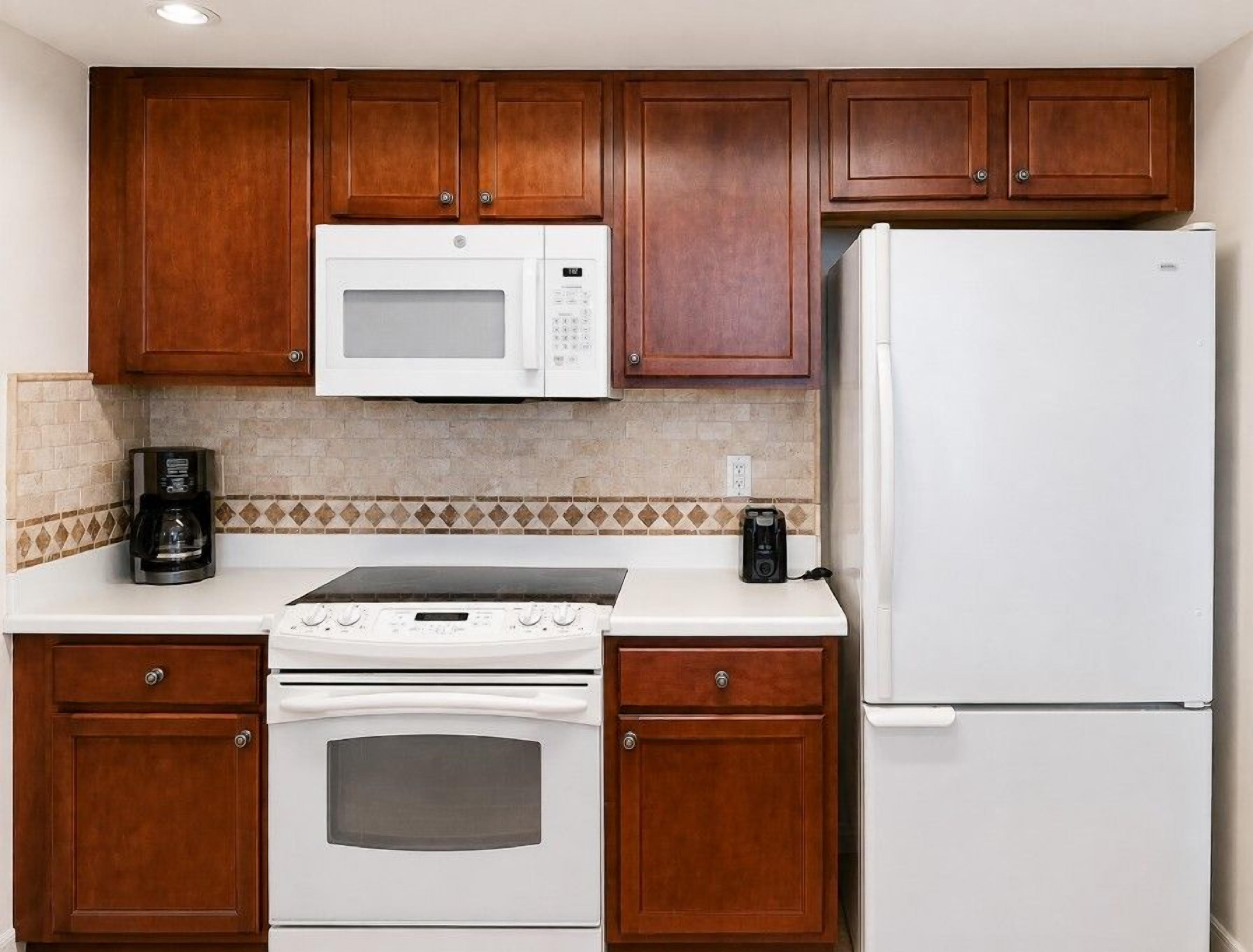 A kitchen with wooden cabinets, a white microwave, a white refrigerator, a stove, and a coffee maker.