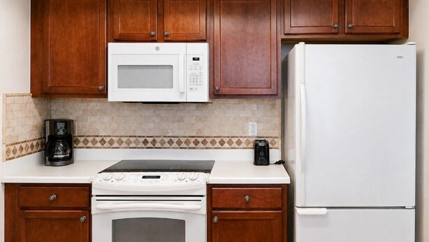 A kitchen with wooden cabinets, a white microwave, a white refrigerator, a stove, and a coffee maker.