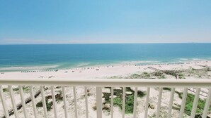 Une vue sur la plage depuis un balcon doté d’une balustrade, avec une plage de sable et l’océan en toile de fond.