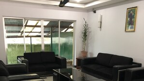 Un espace de bureau moderne avec des canapés en cuir noir, une table basse en verre et un ventilateur de plafond.