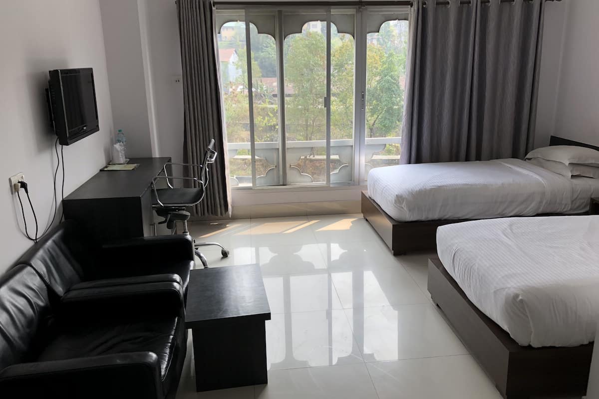 A hotel room with a sofa, a small table, a TV mounted on the wall, a bed, and a window with curtains.