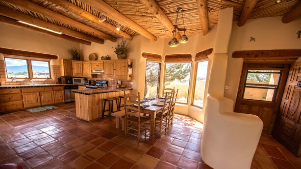 Een ruime keuken met houten kastjes, een eethoek met tafel en stoelen, en grote ramen met uitzicht op de omgeving.