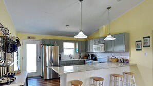 A kitchen with a central island, bar stools, stainless steel appliances, and a breakfast bar. - Bella Beach House | Pet Friendly + Beach Access! (North Topsail Beach)