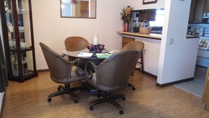 Un comedor con una mesa redonda, cuatro sillas de mimbre, un aparador de cristal y una cocina al fondo.