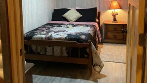 Un dormitorio con techo de madera, una cama con ropa de cama floral, una mesita de noche con lámpara y dos cuadros colgados en la pared.
