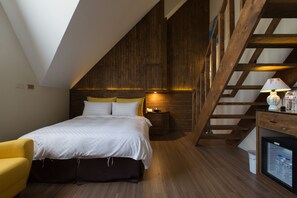 A bedroom with a sloped ceiling, wooden walls, a bed with white bedding, a nightstand, a lamp, and a small refrigerator. - Puli story house (Puli)
