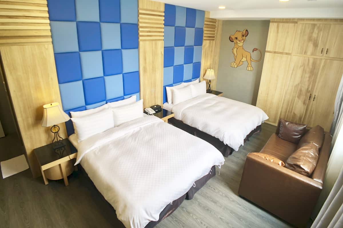 Hotellihuone, jossa on kaksi sänkyä, ruskea nahkasohva, puinen vaatekaappi ja seinämaalaus.