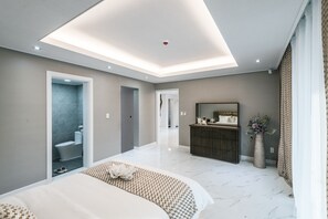 A modern bedroom with a large bed, a vanity with a mirror, and a walk-in closet.