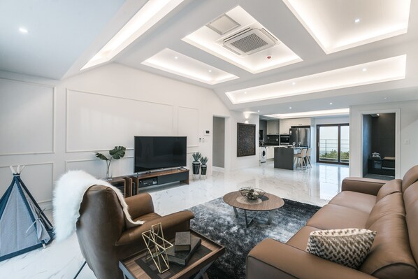 Una sala de estar moderna con un televisor de pantalla plana, sofás de cuero, una mesa de centro y un comedor al fondo.
