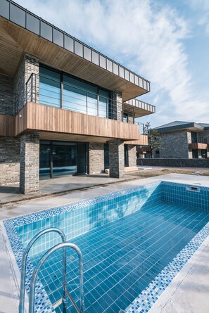 A modern building with a swimming pool, featuring a wooden deck and a brick facade.