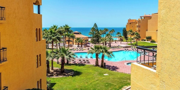 Ein Resort mit einem zentralen Pool, Palmen und Blick auf den Ozean.