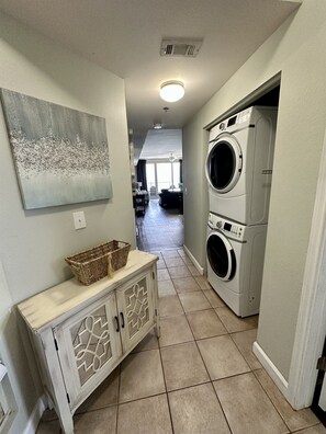 A laundry room with two front-loading washers and dryers, a basket on a cabinet, and a painting on the wall. - Gulf-Front Corner 3BR w/ Wrap Balcony + Sunset Views | Beach service included (Panama City Beach)