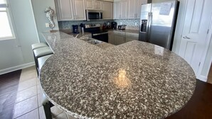 Eine Küche mit Granit Arbeitsplatten, Edelstahlgeräten und weißen Schränken.