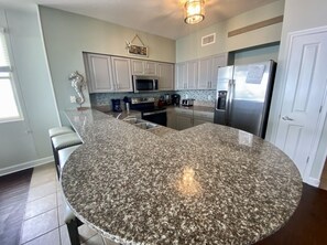 A kitchen with granite countertops, stainless steel appliances, and white cabinetry. - Gulf-Front Corner 3BR w/ Wrap Balcony + Sunset Views | Beach service included (Panama City Beach)
