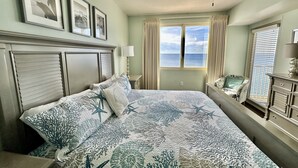 Ein Schlafzimmer mit einem Bett, Deckenventilator, einem fenster mit Vorhängen und gerahmten Bildern an der Wand.