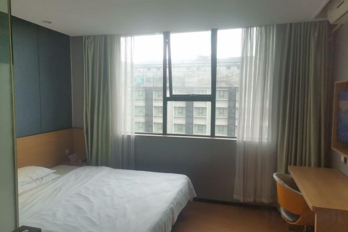 Une chambre d’hôtel avec un lit, un bureau, une chaise et une fenêtre avec des rideaux.