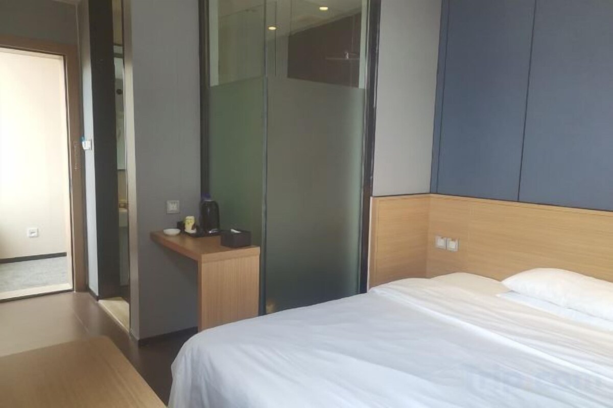 A hotel room with a bed, a bedside table with a coffee maker, a mirror, and a wardrobe.