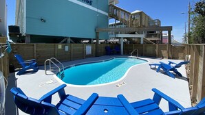 Uma área de piscina com cadeiras de descanso azuis, um deck de madeira e um edifício com a placa 'Sunrise Village'.