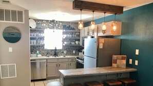 Uma cozinha com ilha central, banquetas, geladeira e janela com vista.