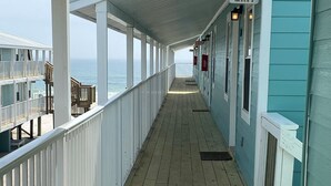 Um deck de madeira coberto com vista para o oceano, uma placa indicando uma saída e um edifício com revestimento azul-turquesa.