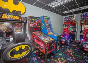 Una habitación con juegos de arcade, incluyendo una máquina temática de Batman, y un suelo con un estampado de estrellas coloridas.