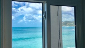A view through a window with a clear sky and turquoise sea. - CASA CARIBE OCEANFRONT TWO STORY LOFT VILLA, Air Conditioning, Beautiful Views. (Little Apple Bay)