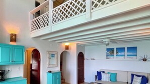 A spacious living area with a high ceiling, a balcony with a lattice railing, and a dining area with turquoise cabinets. - CASA CARIBE OCEANFRONT TWO STORY LOFT VILLA, Air Conditioning, Beautiful Views. (Little Apple Bay)