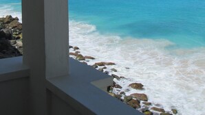 A coastal view with clear blue water, a rocky shoreline, and a distant mountain range. - CASA CARIBE OCEANFRONT TWO STORY LOFT VILLA, Air Conditioning, Beautiful Views. (Little Apple Bay)
