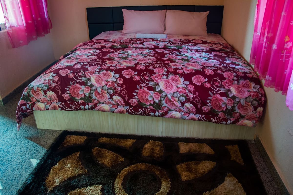 A bed with a floral bedspread, a headboard, and a patterned rug.